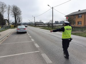 zdjęcie przedstawia umundurowanego policjanta ruchu drogowego stojącego na jezdni, który daje sygnał nadjeżdżającemu pojazdowi do zatrzymania, przy pomocy tarczy do zatrzymywania pojazdów
