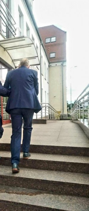 Zdjęcie przedstawia jednego z oszustów w drodze do Sądu Rejonowego w Gryficach , mężczyzna ubrany w niebieski garnitur na rękach ma kajdanki.