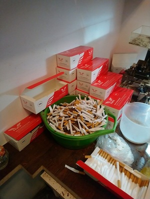 Zdjęcie przedstawia Gilzy do produkcji papierosów oraz pudełka znanej marki papierosów w tym pudełka zbiorcze. Przedmioty zostały zabezpieczone na miejscu zdarzenia.