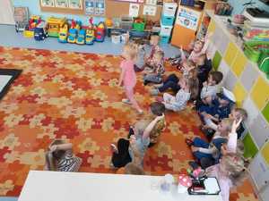 Na zdjęciu widać dzieci, które siedzą w sali na dywaniku i biorą aktywny udział w spotkaniu z Policjantami dzieci mają podniesione ręce na znak chęci zabrania głosu.