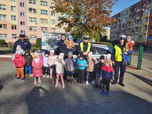 Zdjęcie przedstawia dzieci z Przedszkola nr 1 w Gryficach podczas pamiątkowego zdjęcia z Policjantami Ruchu Drogowego z Gryfic na placu przedszkola przy oznakowanym radiowozie policyjnym.