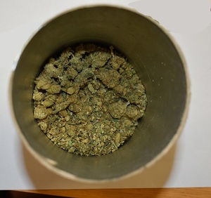 Zdjęcie przedstawia pojemnik z zawartością suszu roślinnego tj. marihuany.