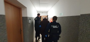 Zdjęcie przedstawia jednego ze sprawców kradzieży w czasie konwojowania do Aresztu Śledczego w Szczecinie. Mężczyzna idzie prowadzony przez dwóch umundurowanych Policjantów korytarzem w KPP w Gryficach