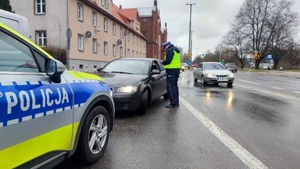 Zdjęcie poglądowe. Na zdjęciu widać umundurowanego policjanta ruchu drogowego podczas kontroli drogowej, w tle widać ulicę i budynki. Zdjęcie nie przedstawia opisywanej sytuacji w komunikacie.